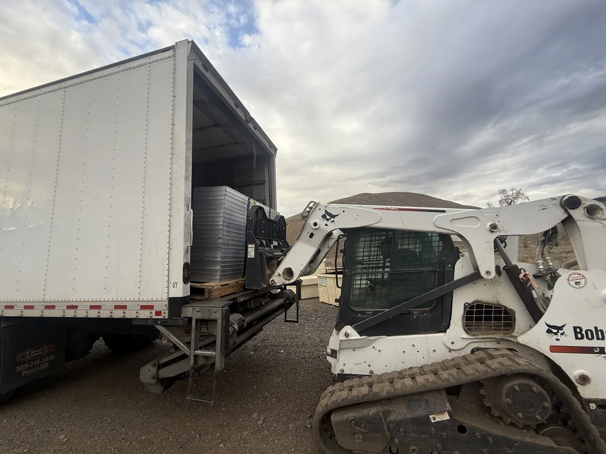 Palletized solar panels being loaded into a truck with a compact loader.